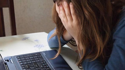 A photo of a woman cupping her face while sitting across her laptop