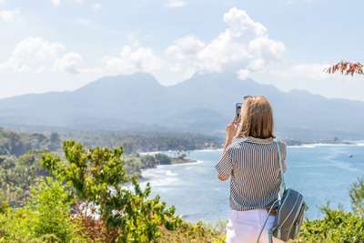 A woman taking a picture of the beautiful scenery on top of a hill.