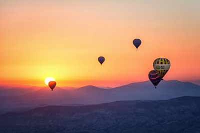 Hot air balloons flying across the horizon on a sunset.